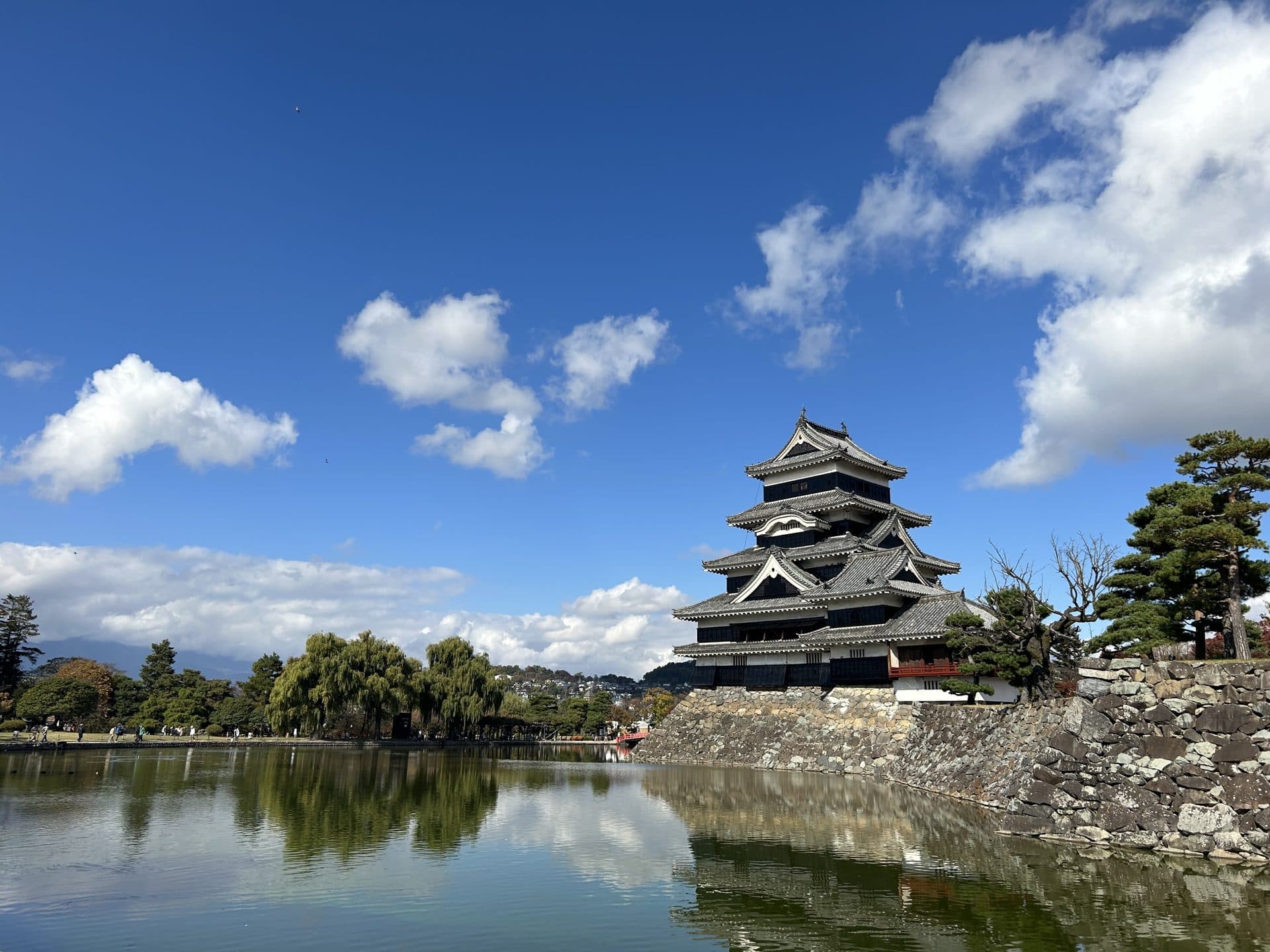 The black keep of Matsumoto Castle reflected in its moat beneath a bright blue sky